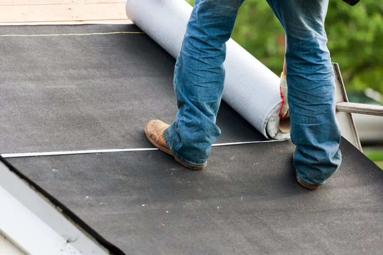 Roofer rolling out underlayment across a roof deck during installation in Havre de Grace, MD