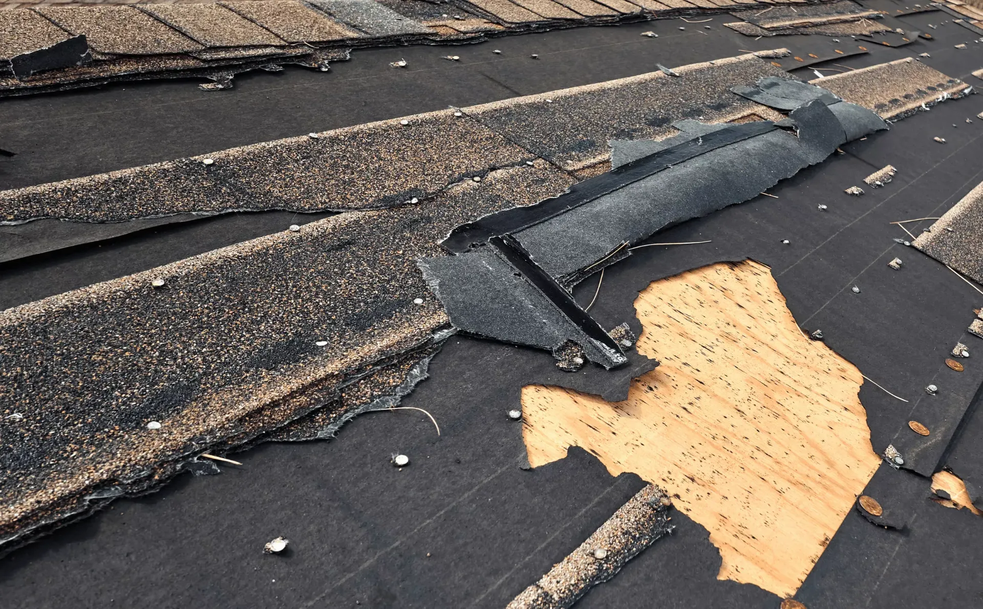 Storm-damaged roof in Maryland with torn shingles and exposed wood decking