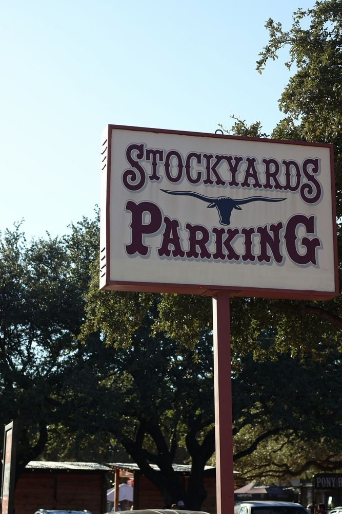 Stockyards Parking sign with longhorn graphic, against a blue sky, trees in the background.
