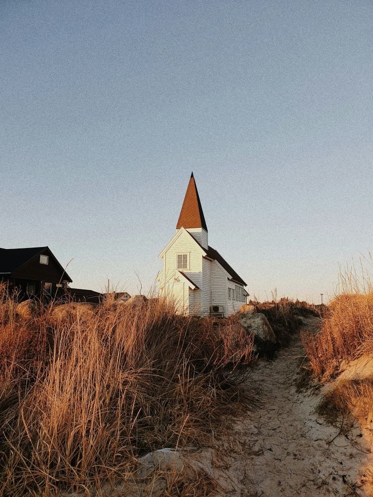 White church with a brown steeple on a hill with tall, dry grass against a clear blue sky.