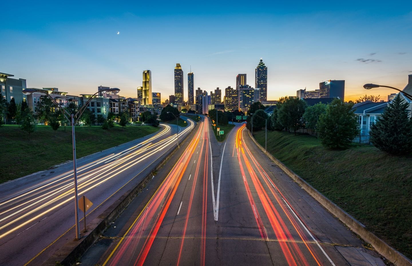 City skyline at dusk with highway traffic streaks, blue sky.