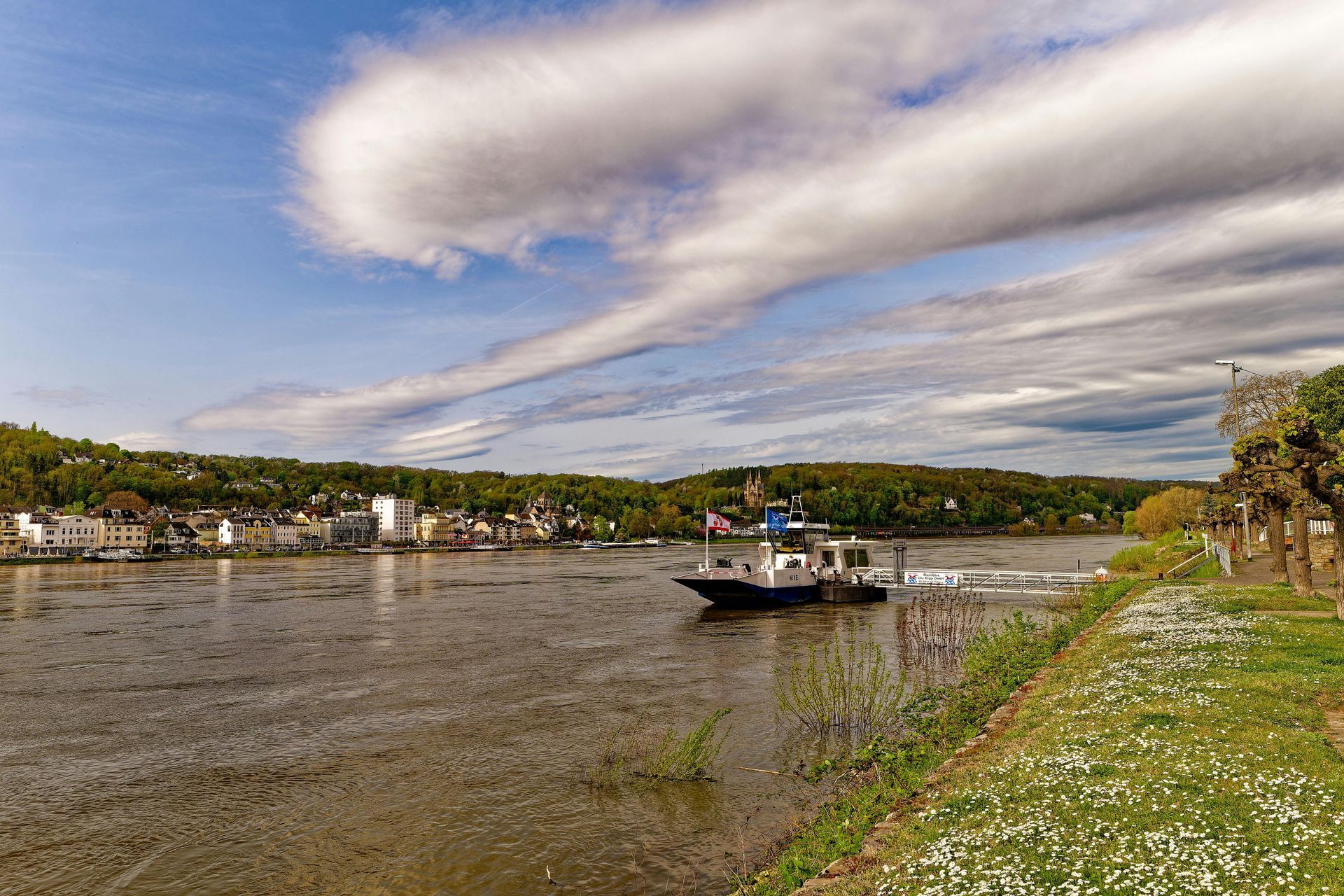 River cruise ship sails past a hillside village. Houses on a green, wooded slope.