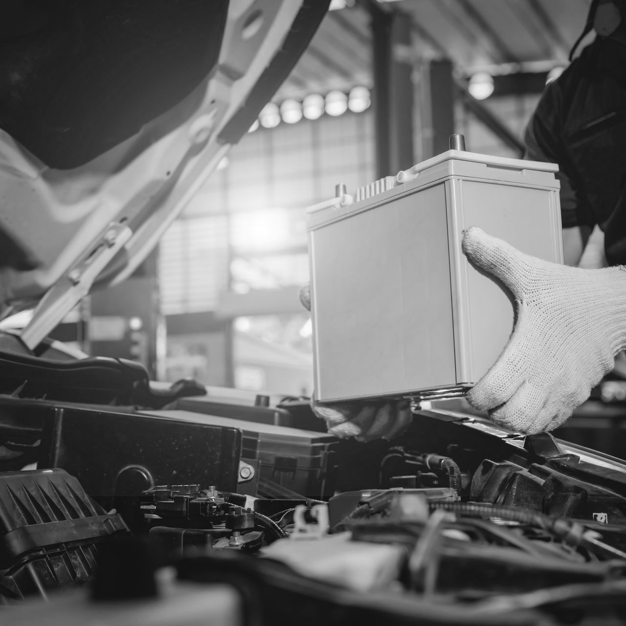 Gloved worker lifts a box into a car engine bay in an auto repair shop