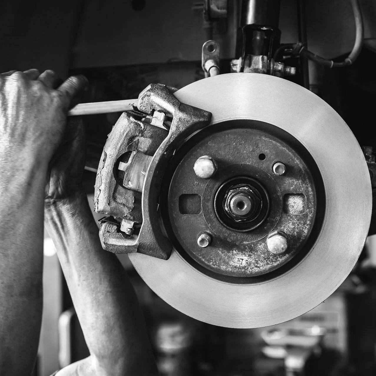 Mechanic working on a car brake rotor and caliper with a tool in a garage