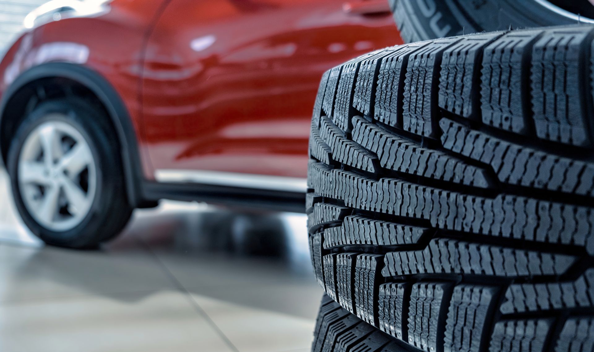 Close-up of a tire with tread, red car in background.