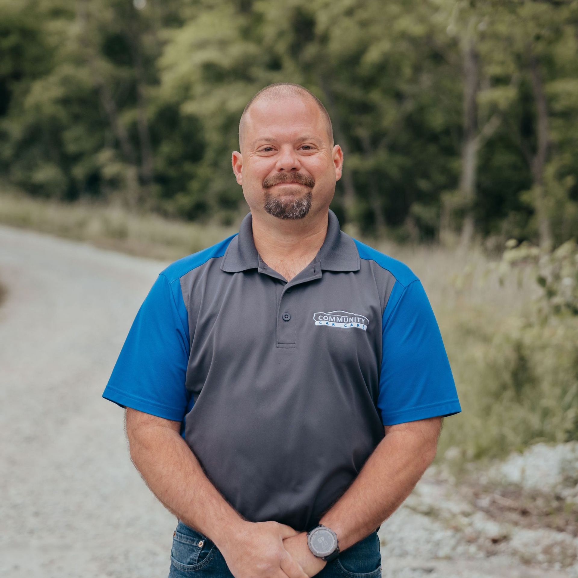 Smiling man in a gray and blue polo shirt standing outdoors on a rural road