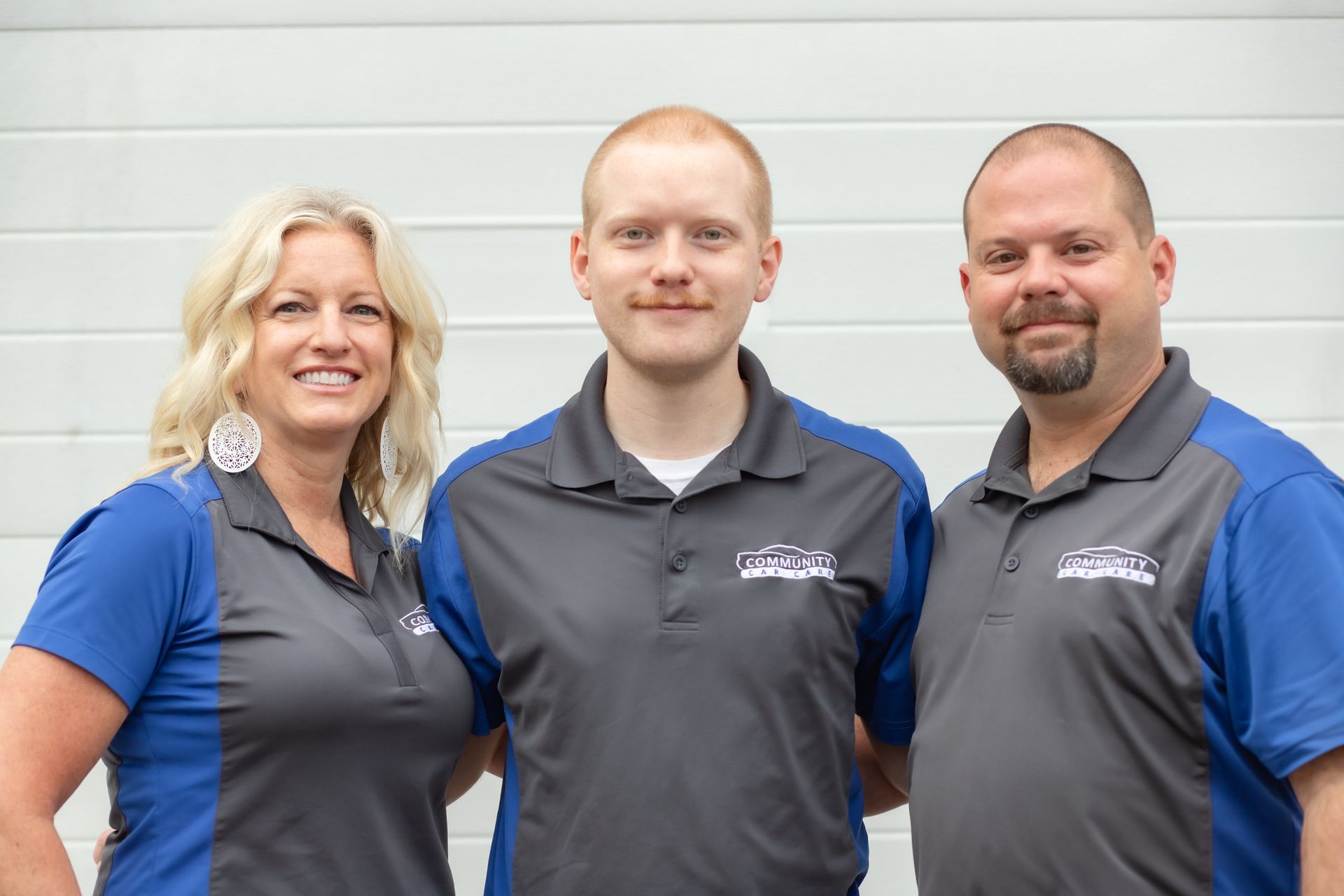 Three people in gray and blue work shirts standing in front of a light wall