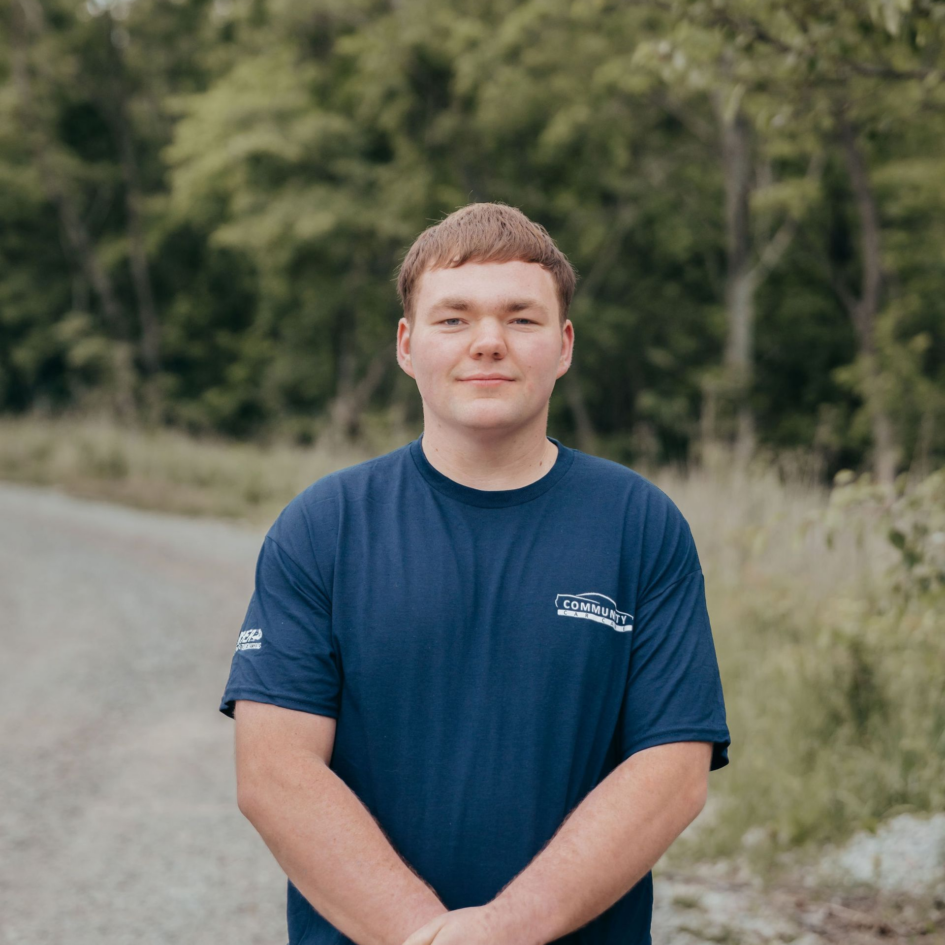 Person standing on a gravel road with trees in the background, wearing a navy T-shirt.