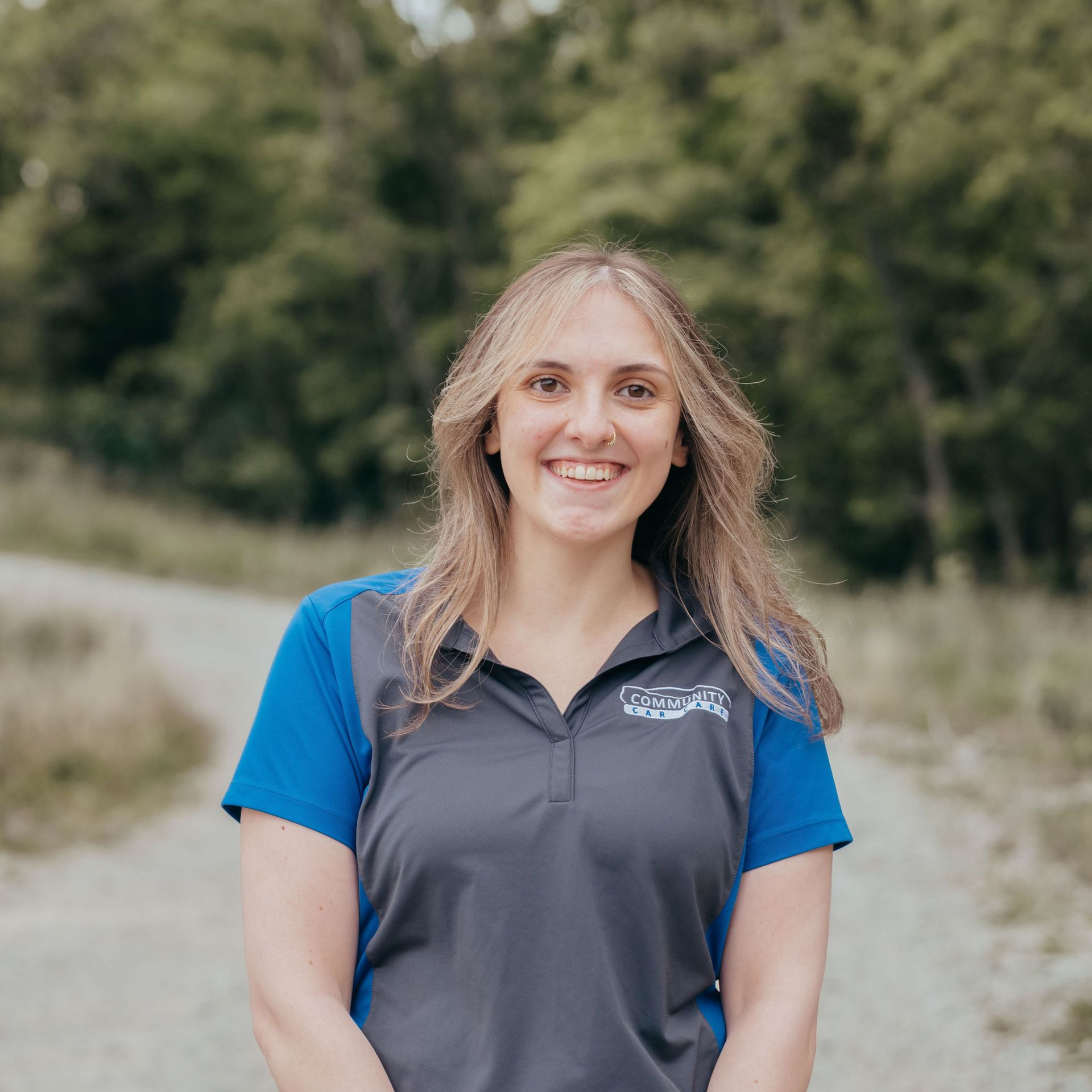 Smiling person in a blue and gray polo standing outdoors with a blurred green background