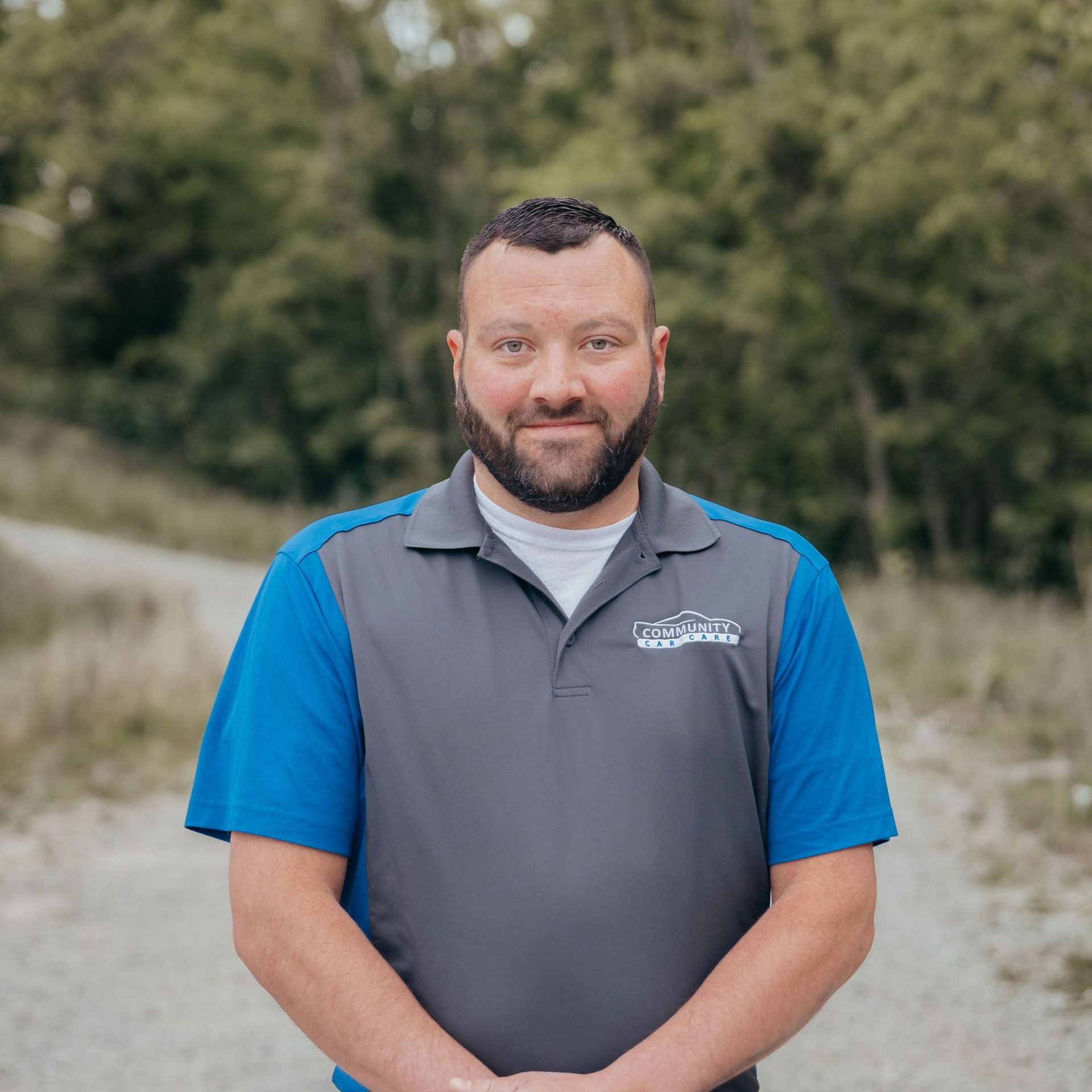 Man standing outdoors in a blue and gray polo shirt with hands clasped in front of him