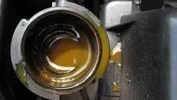 Open car coolant filler neck, containing discolored, oily fluid.