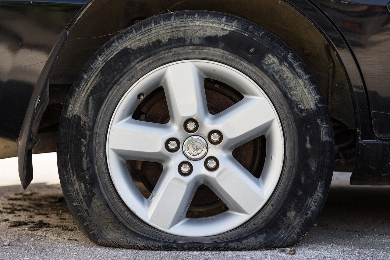 Flat tire on a black car with a silver wheel, parked on gravel.