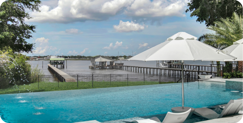 Infinity pool overlooking a body of water with docks, white umbrellas, and a cloudy sky.