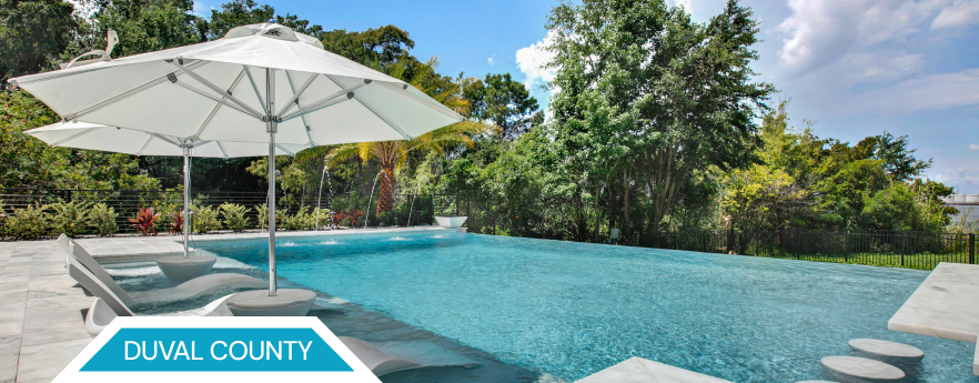 A pool with a white umbrella, surrounded by trees, with