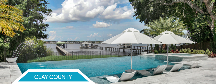 Clay County waterfront property with a pool and umbrellas overlooking a body of water.