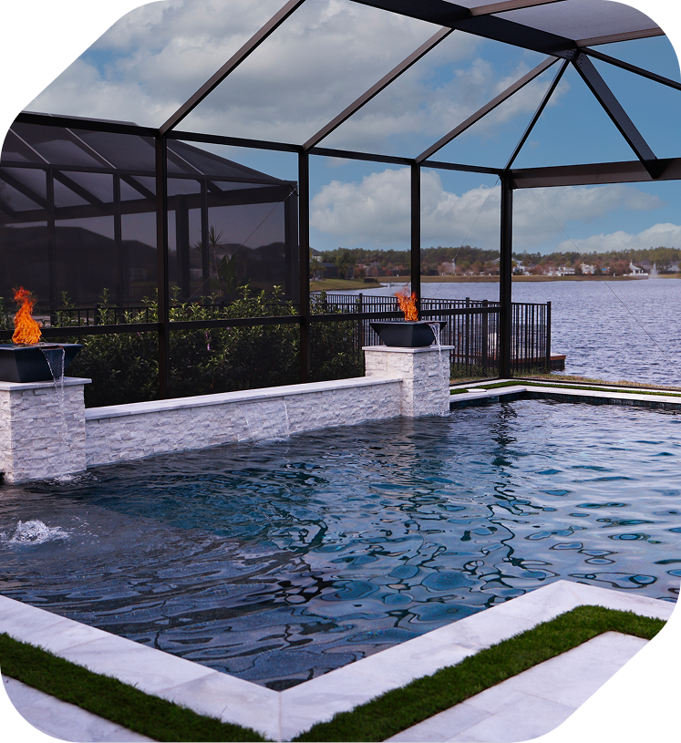 An indoor pool with a stone wall and two fire bowls, enclosed by a screen structure overlooking a lake.