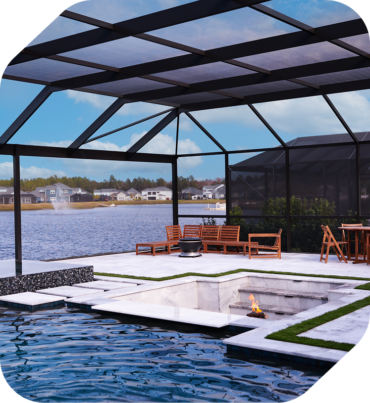A swimming pool with an integrated sunken fire pit on a stone patio inside a screened lanai overlooking a lake.