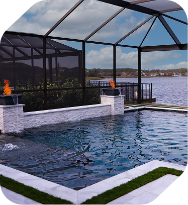 A pool with a stone water feature and fire bowls, enclosed in a screened lanai overlooking a lake.