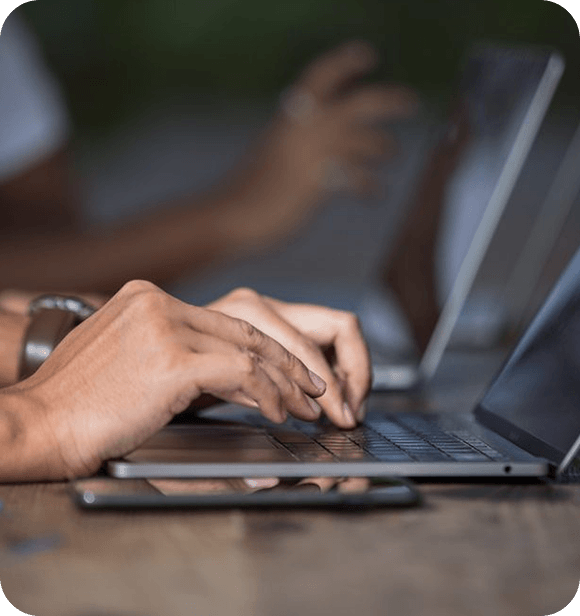 Hands typing on a laptop with a smartphone on the table in a blurred indoor setting