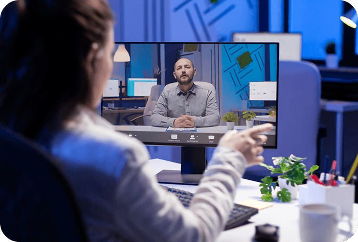 Virtual meeting on a monitor in a modern office, with a person speaking to the camera.