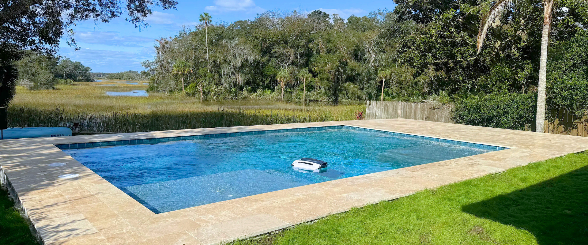 Outdoor swimming pool with blue water, a floating cleaner, and grassy yard with trees in the background