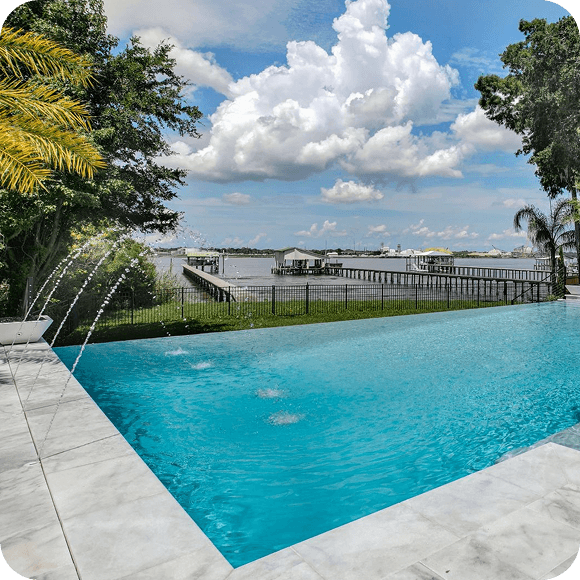 Infinity pool overlooking a waterfront dock under a bright blue sky with large white clouds