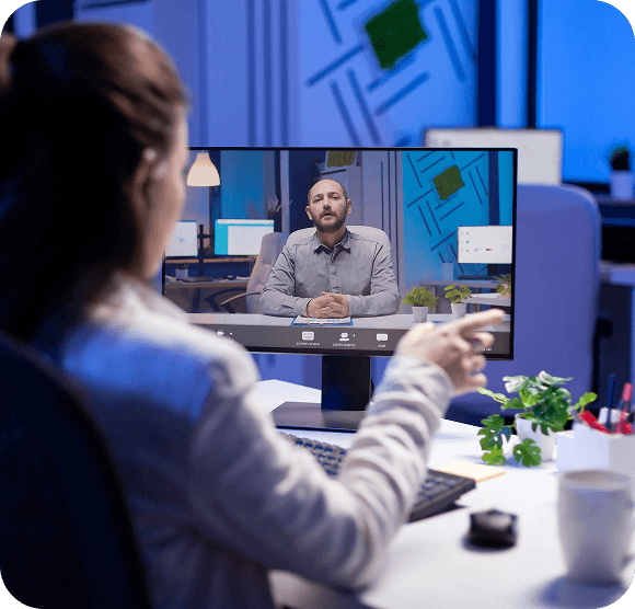 Virtual meeting on a monitor in a modern office, with a person speaking to the camera.