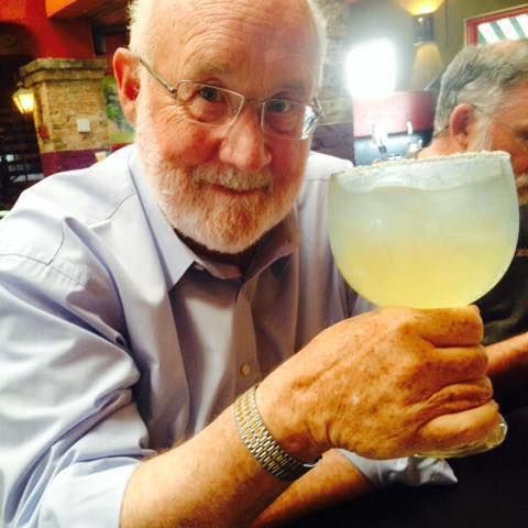 A man with glasses is holding a glass of liquid in his hand