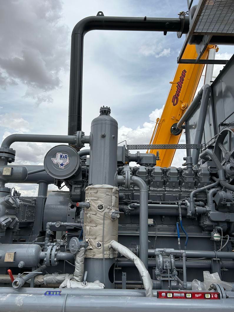 A close up of a machine with pipes and a crane in the background.