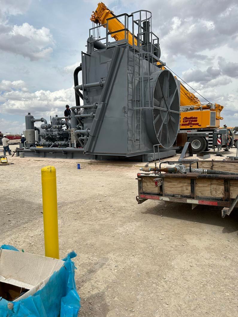 A large machine is sitting on top of a dirt field next to a truck.