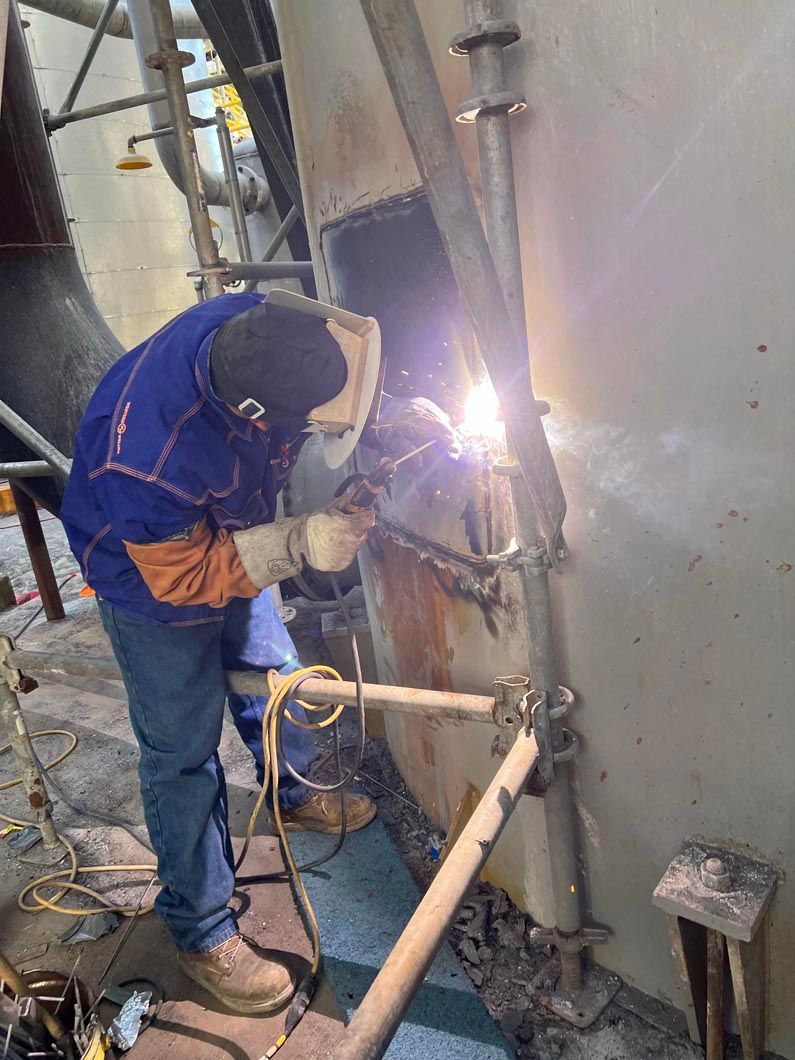 A man is welding a pipe in a factory.