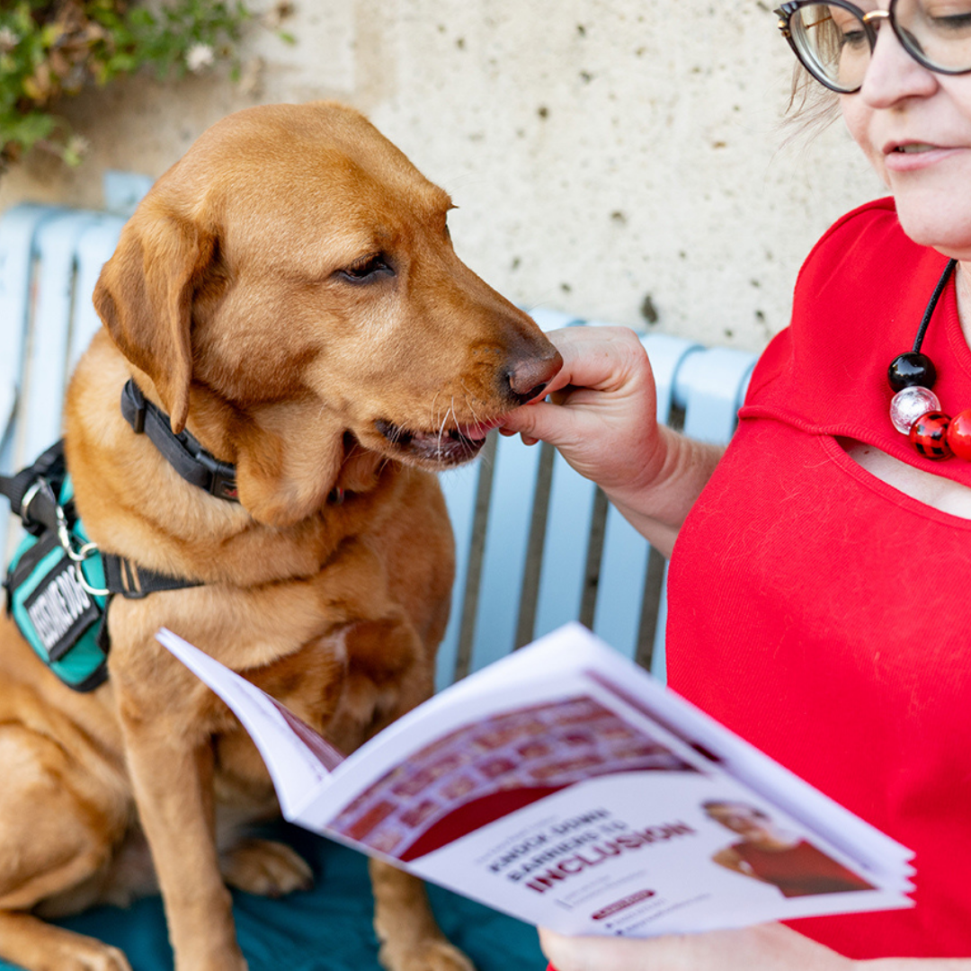 Image of an individual reading an inclusion booklet from the Easy Read Toolbox while giving their service dog a treat.