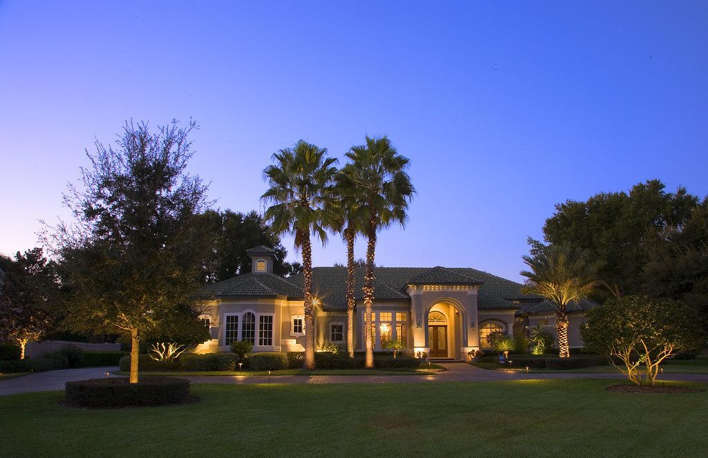Twilight view of a lit Mediterranean-style mansion with palm trees and a manicured lawn