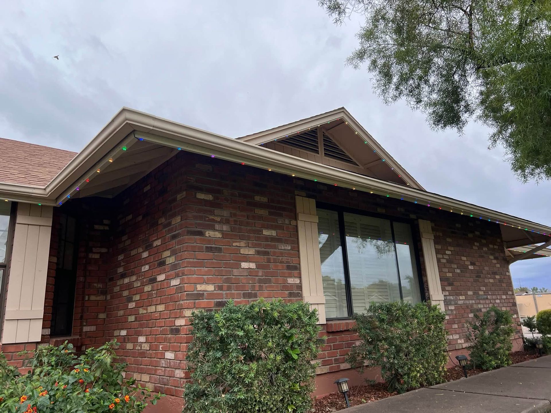 Brick house exterior with large windows, shrubs, and a cloudy sky
