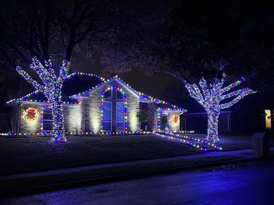 House decorated with colorful holiday lights at night, with illuminated trees in front yard.