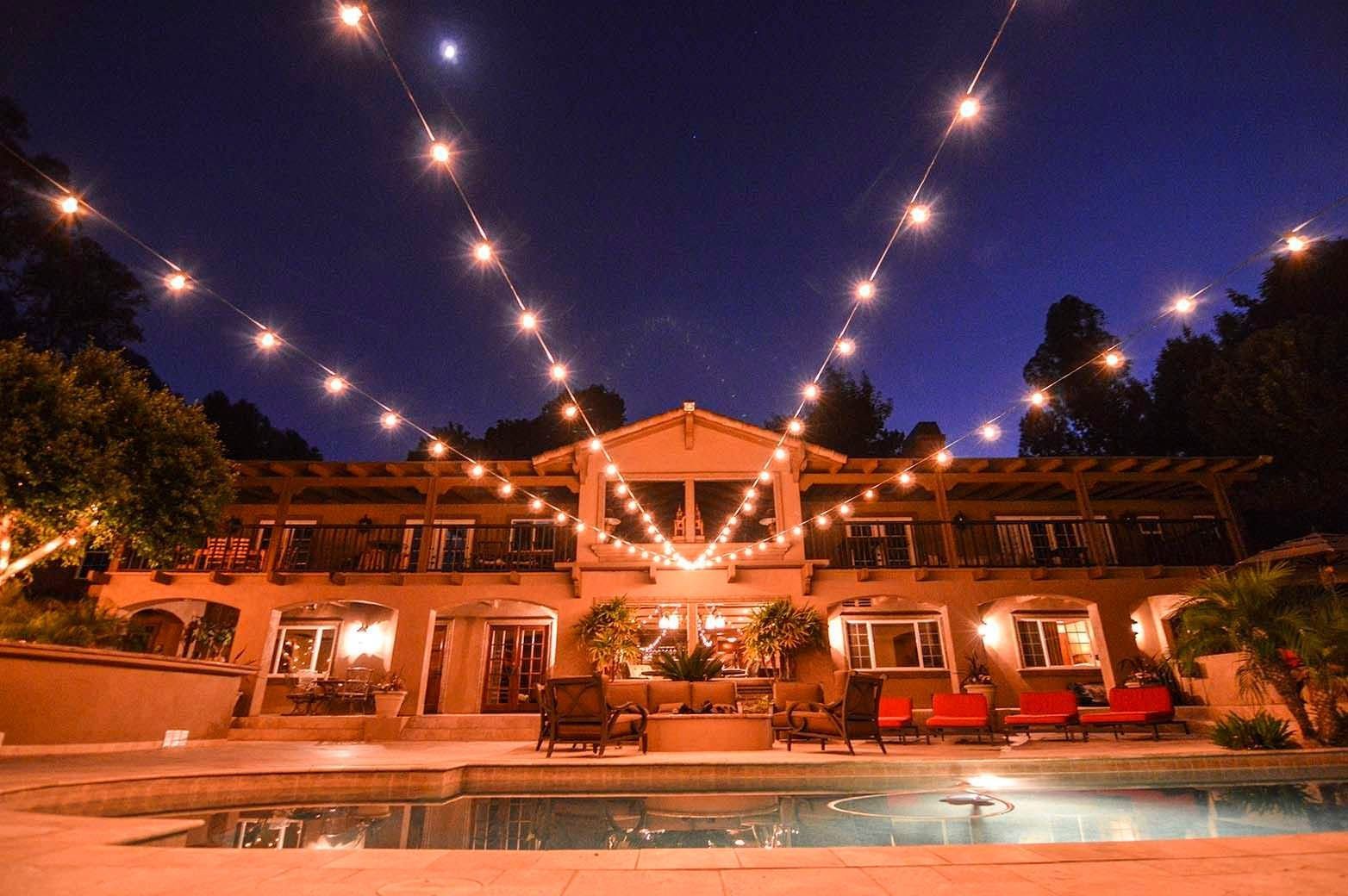 Night-lit resort poolside terrace with string lights and a warmly lit building at dusk