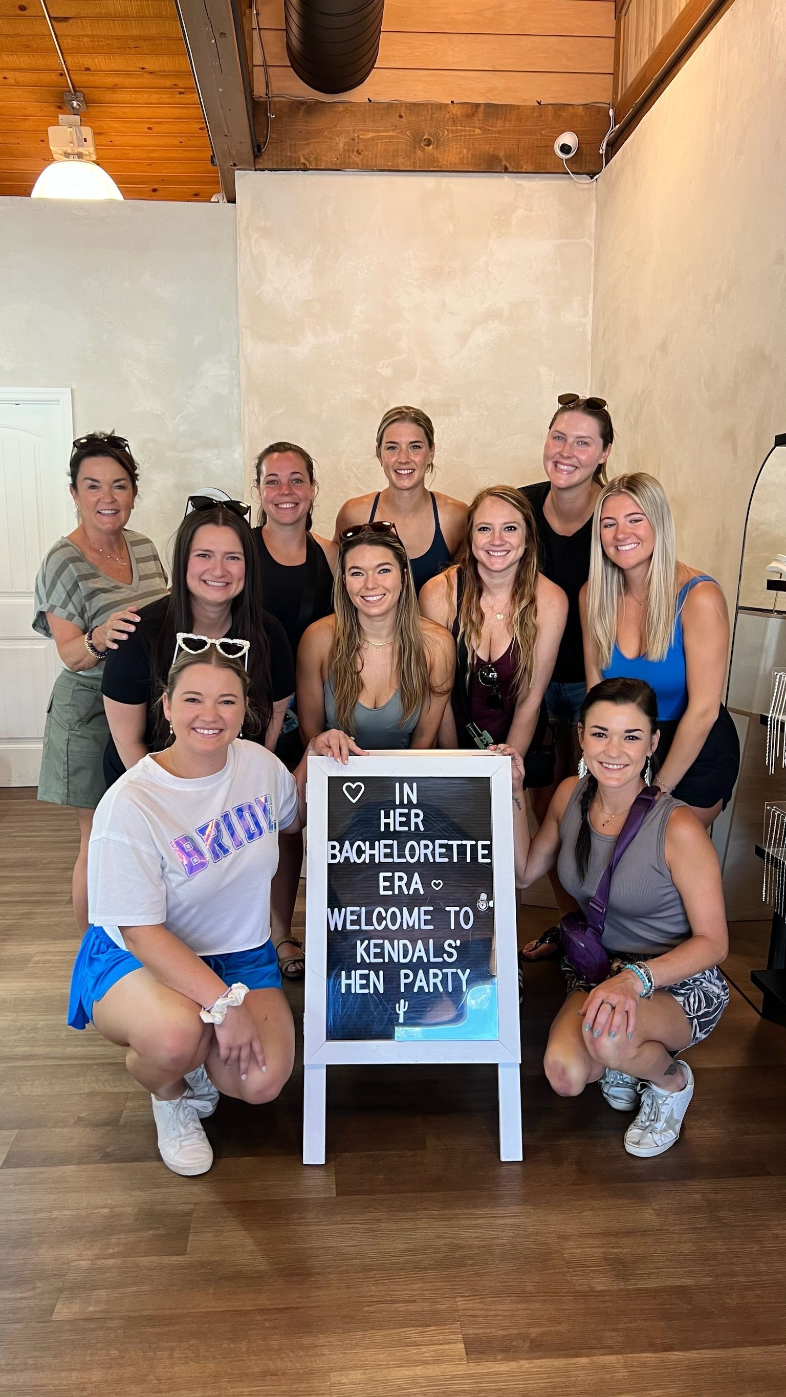 Group posing indoors around a chalkboard sign in a rustic room, smiling at the camera.