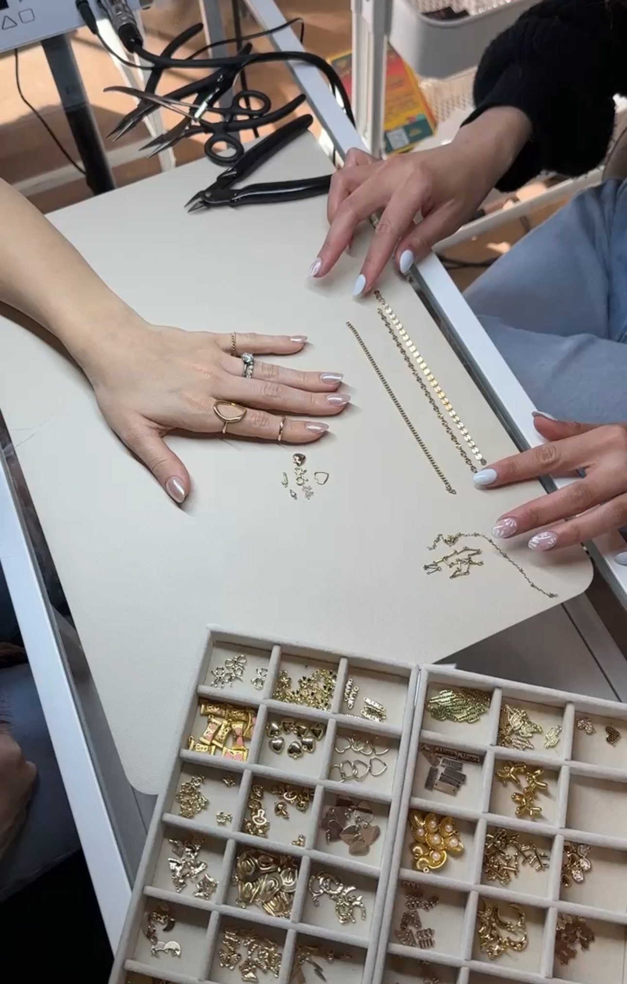 Hands arranging beads and jewelry components on a worktable with organized trays below.