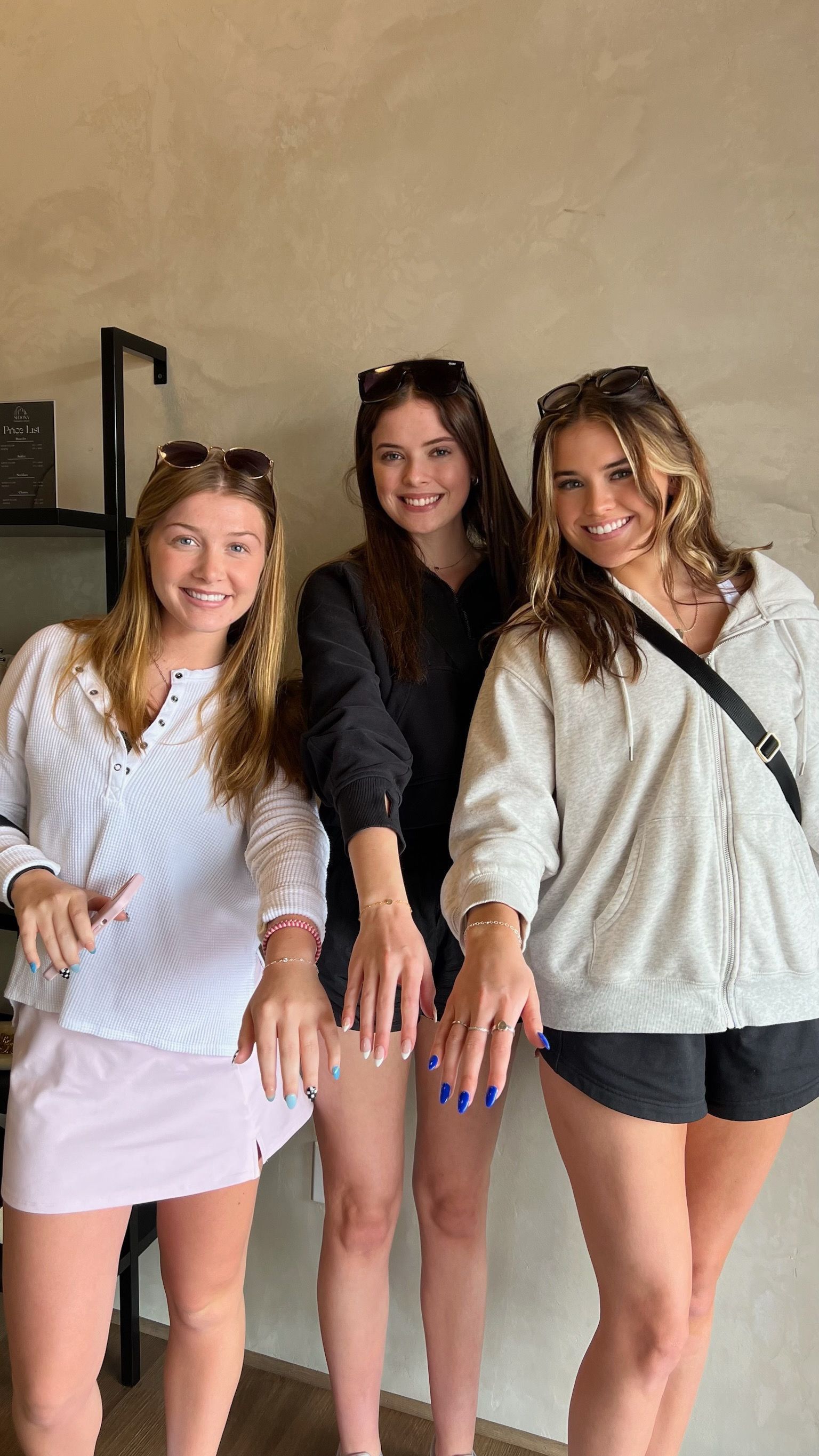 Three friends posing indoors, smiling and leaning toward the camera in casual clothes.