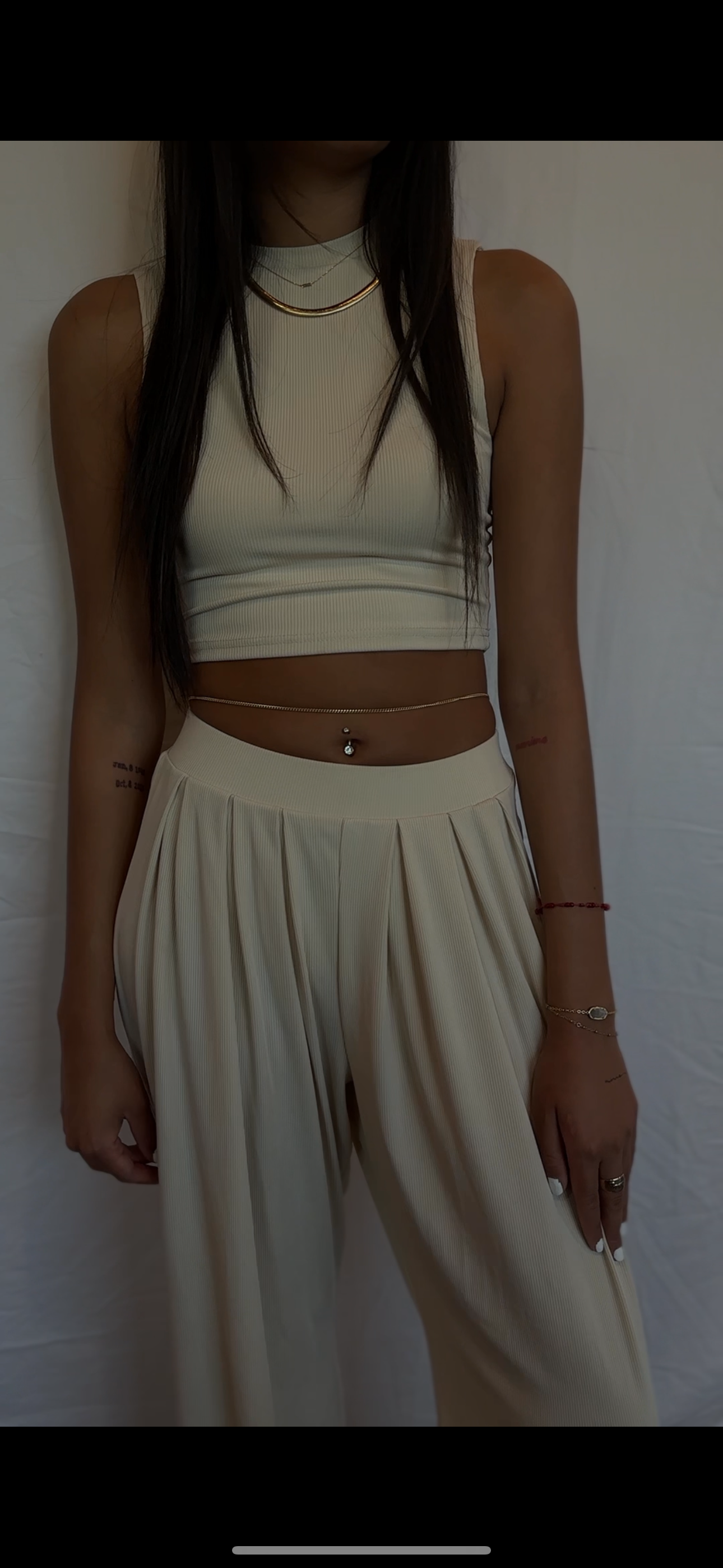 Person standing indoors in a white crop top and matching pants against a plain wall