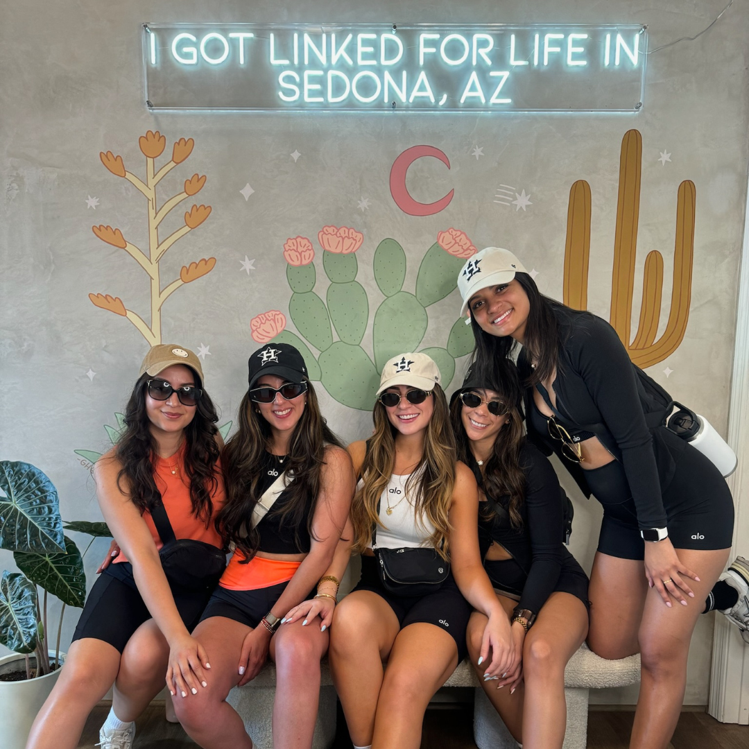 Five friends posing on a couch before a “I GOT LINKED FOR LIFE IN SEDONA, AZ” neon sign and cactus mural