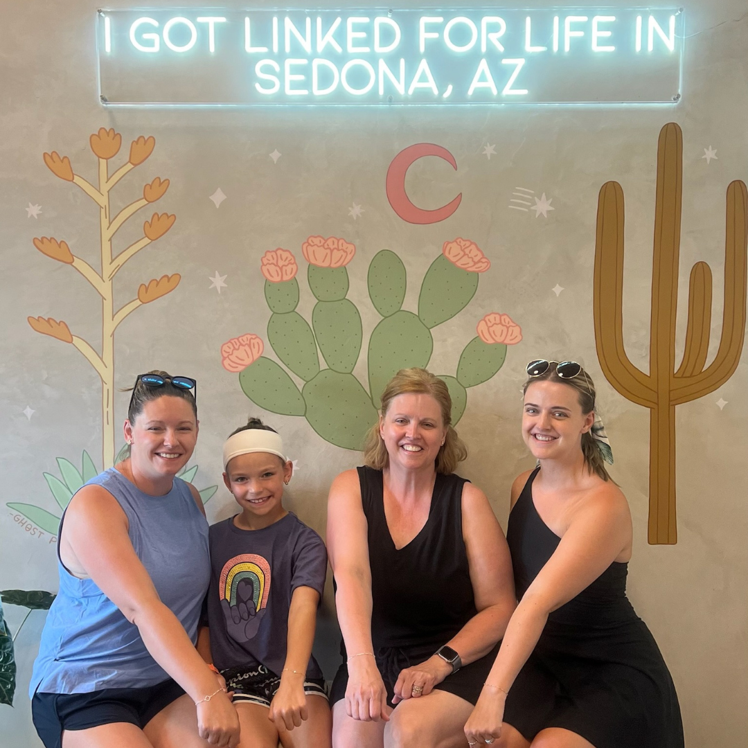 Four people posing in front of a desert mural with cacti and the text “I GOT LINKED FOR LIFE IN SEDONA, AZ.”