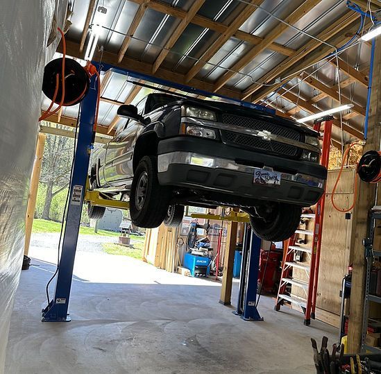 A truck lifted on a blue hydraulic lift inside a workshop.