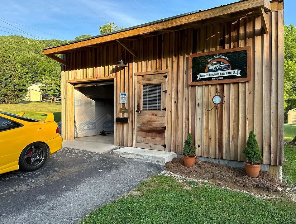 Yellow car parked next to a wooden building with a sign and door, a driveway, and greenery.
