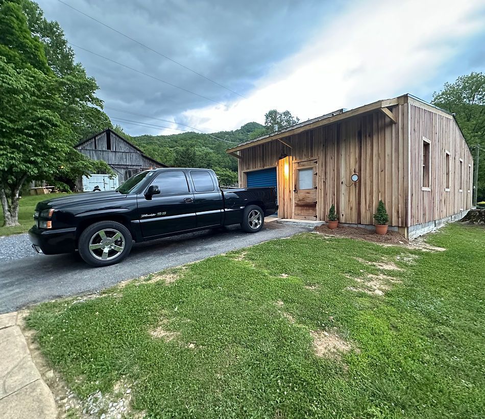 Black truck parked on a driveway in front of a wooden building. Green grass and a mountain in the background.