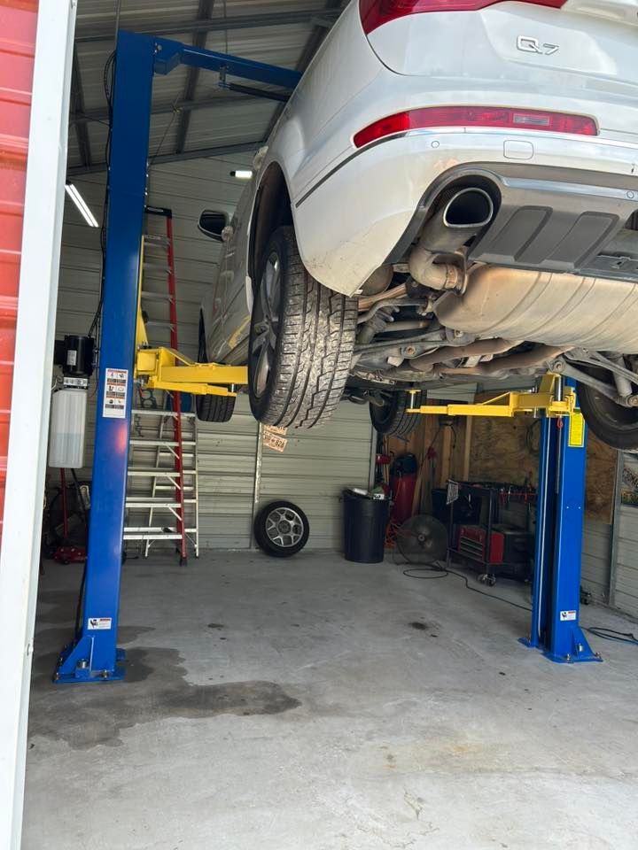 White SUV raised on a two-post lift in a garage. Yellow lift arms support the vehicle.