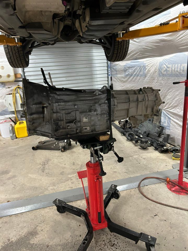 Car being worked on in a garage, transmission is lowered on a jack.