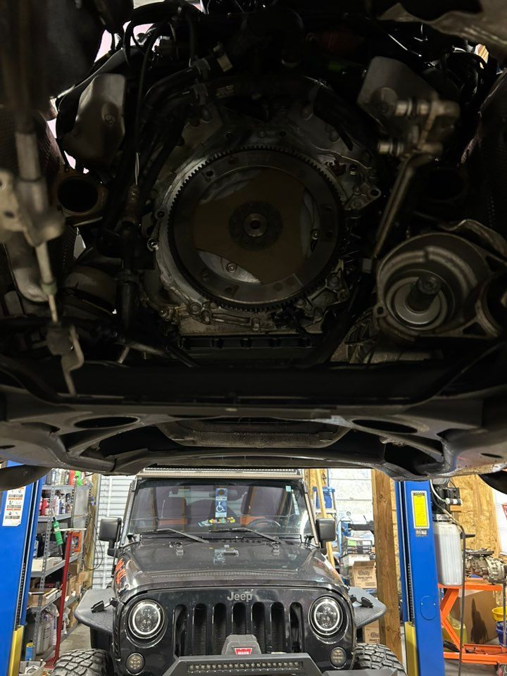 Jeep under car lift; engine and underside visible. Mechanic's shop background.