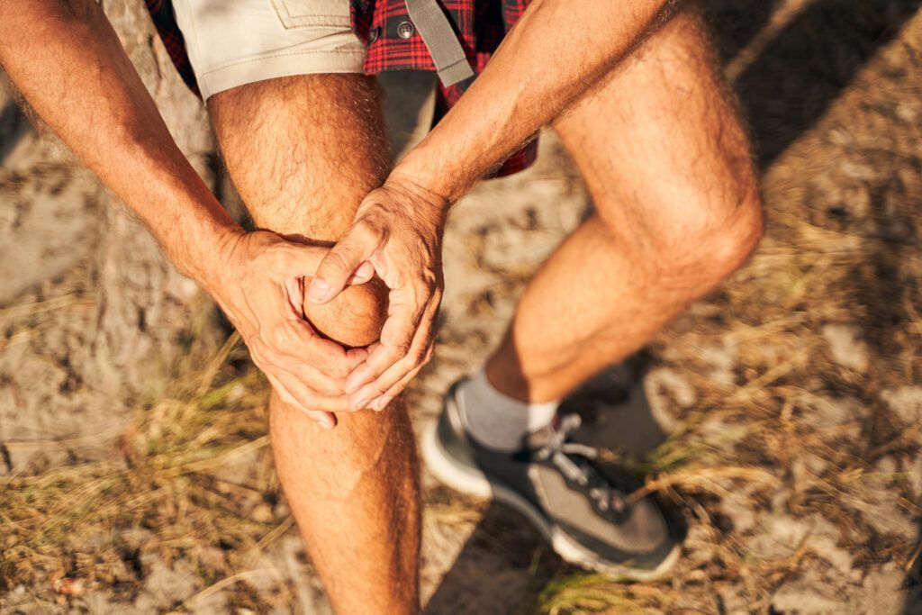A man is holding his knee in pain while sitting on a rock.