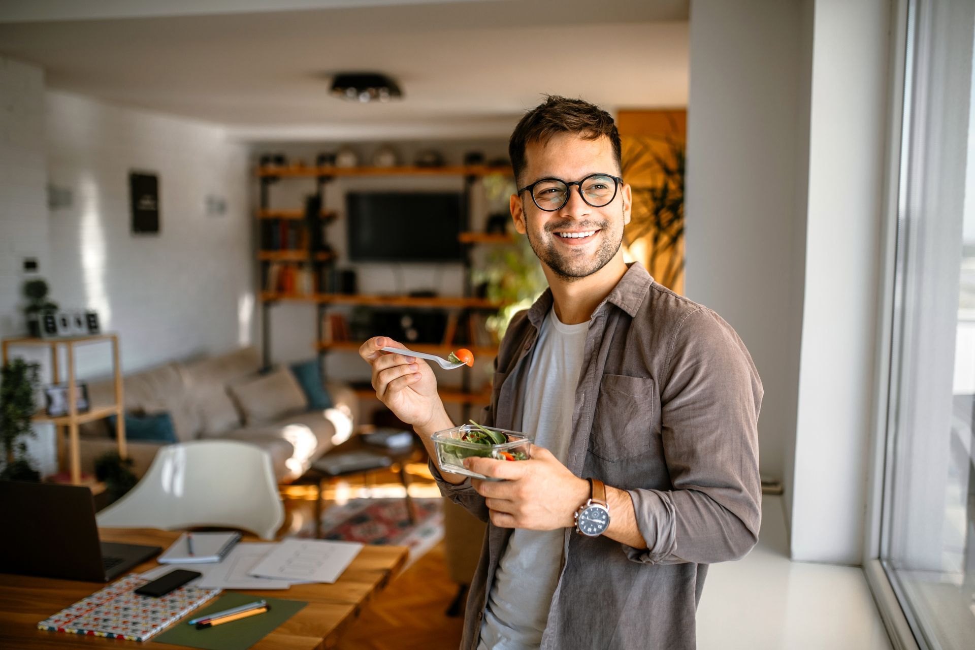 Man eating a salad while looking out a window